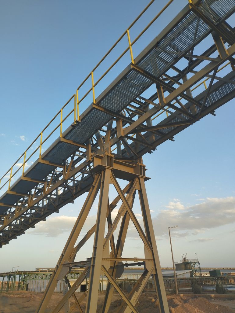 Raised industrial pipe bridge with steel columns and yellow handrails